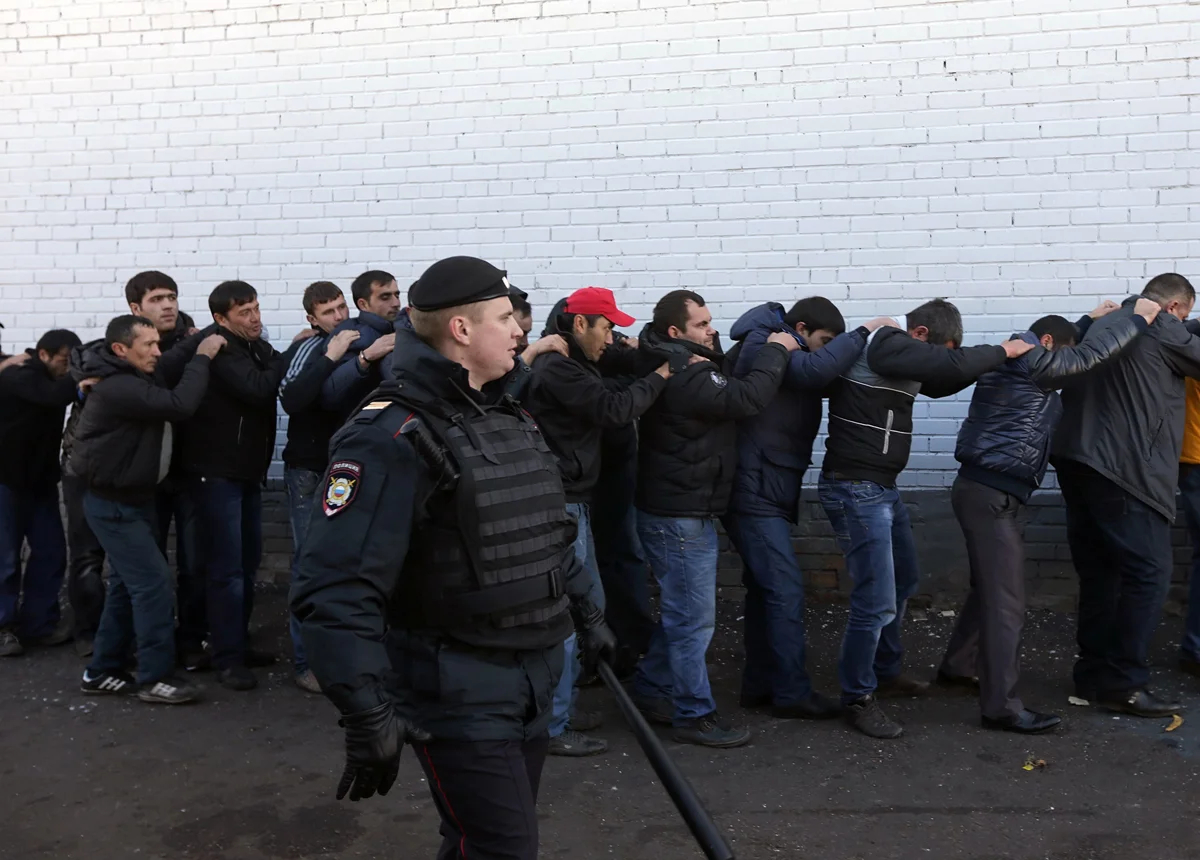 Полицейский стоит рядом с задержанными мигрантами во время рейда на овощном складе в Москве, 14 октября 2013 года. Фото: Максим Шипенков / EPA