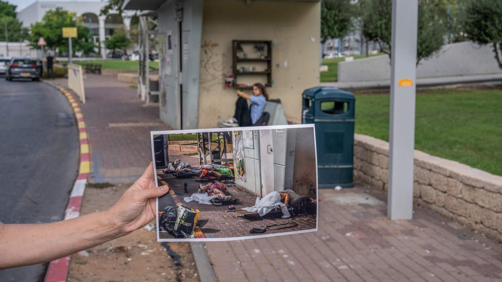 Женщина держит фотографию с изображением тел погибших израильтян на автобусной остановке в Сдероте после атаки боевиков ХАМАС 7 октября 2023 года, на том же самом месте год спустя. Сдерот, Израиль. 26 сентября 2024 года. Фото: Ilia Yefimovich / dpa / Scanpix / LETA