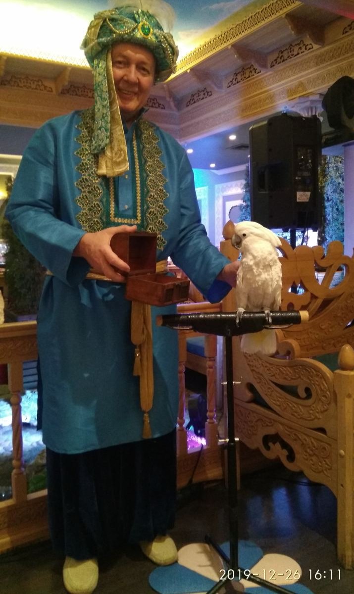 Михаил Жуков перед выступлением стоит в велкам-зоне с попугаем, который тянет для гостей предсказания из коробочки, Москва, 2019 год. Фото предоставлено Александром Жуковым