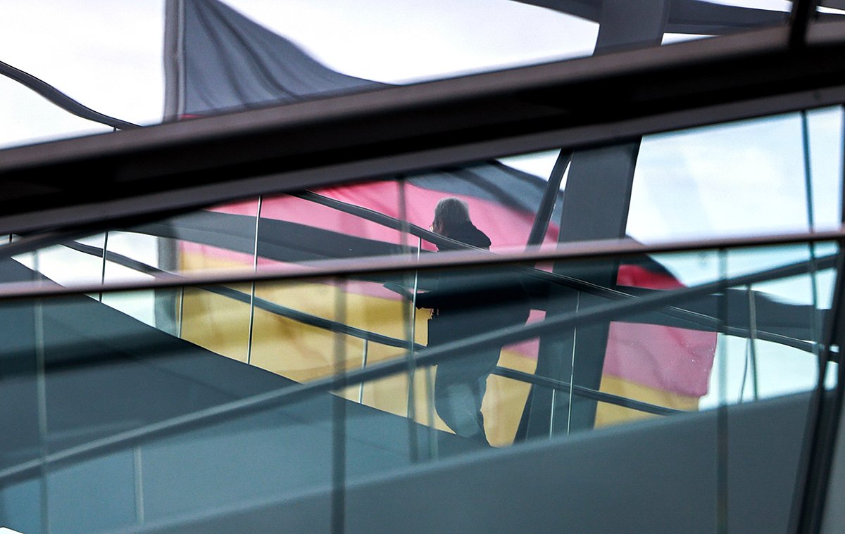 Посетитель проходит мимо немецкого национального флага на куполе здания Рейхстага во время ежегодного стартового заседания расширенного исполнительного совета парламентской группы «Зеленых» в Берлине, 14 января 2025 года. Фото: Hannibal Hanschke / EPA-EFE